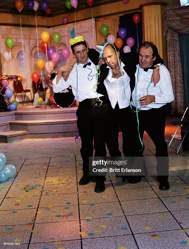 Two men supporting drunken man at party