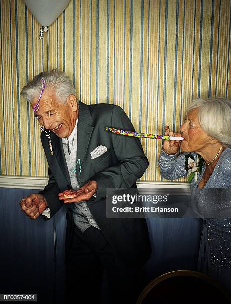 elderly couple, woman blowing party blower at man - matasuegras fotografías e imágenes de stock