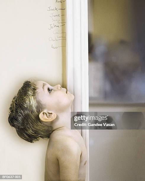 boy (3-5) measuring self against doorway, looking up, profile - groeimeter stockfoto's en -beelden