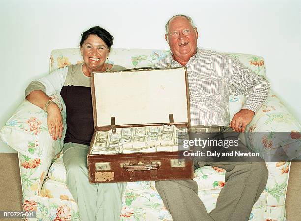 mature couple on sofa with suitcase full of money - men bulge imagens e fotografias de stock