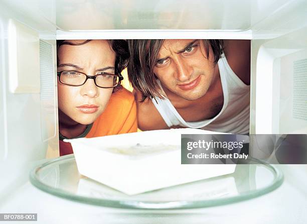 young man and woman looking at microwave meal in microwave - tv dinner stock pictures, royalty-free photos & images