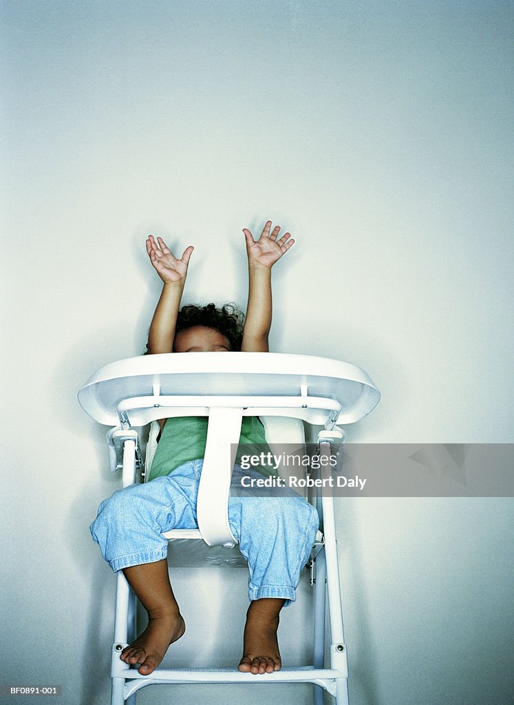 Boy (21-24 months) in highchair, arms raised, low angle view