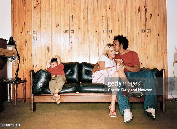 boy (5-7) beside young couple embracing on leather sofa - couple ignore stock pictures, royalty-free photos & images