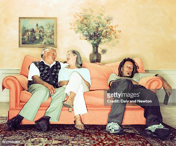 mature couple on sofa beside man holding television remote - exclusion stock-fotos und bilder