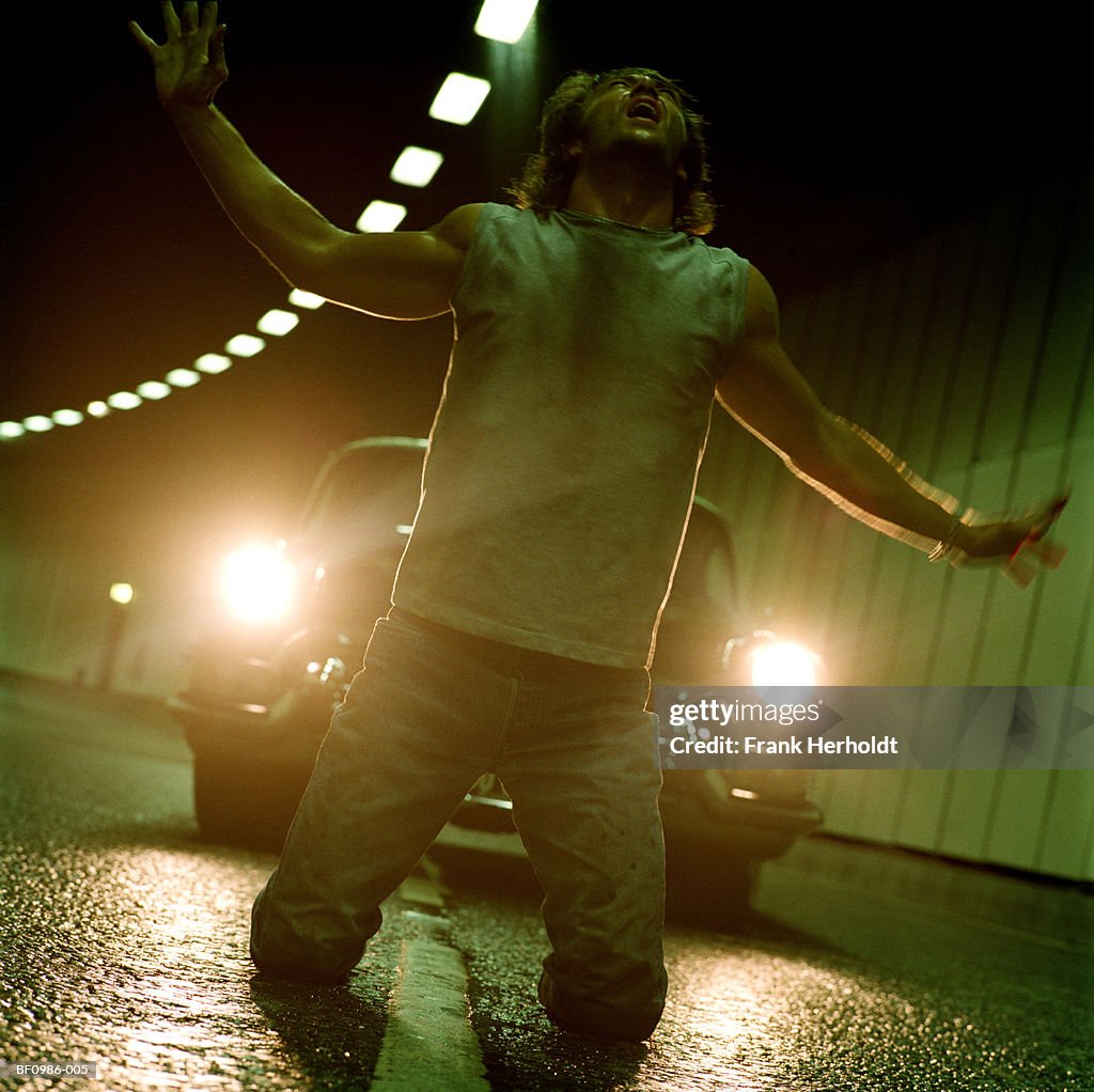 Man kneeling on road in front of car, arms outstretched, close-up