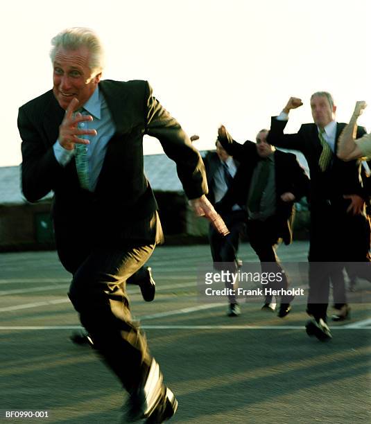 mature businessman running from crowd outdoors (blurred motion) - huir fotografías e imágenes de stock