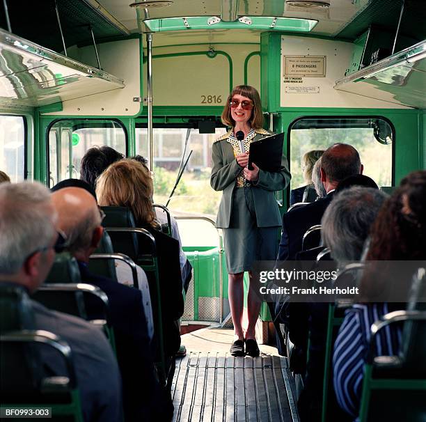 female tour guide with microphone and clipboard on packed bus - reiseführer stock-fotos und bilder