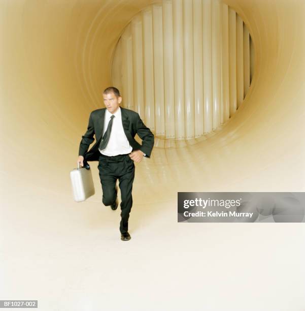 young male executive with briefcase running through wind tunnel - briefcase stock pictures, royalty-free photos & images