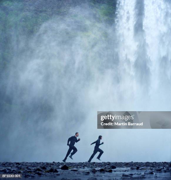 iceland, skogafoss, young couple running in front of waterfall - spåra bildbanksfoton och bilder