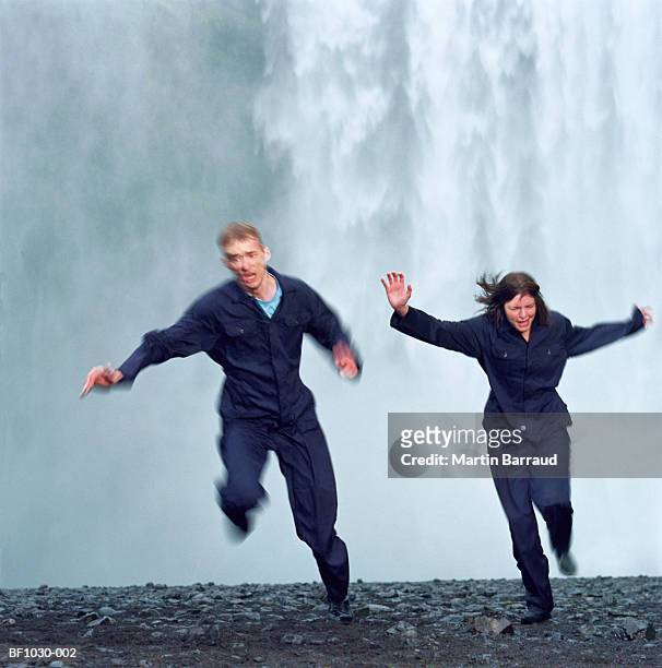 young couple running away from waterfall (blurred motion) - escape stock-fotos und bilder