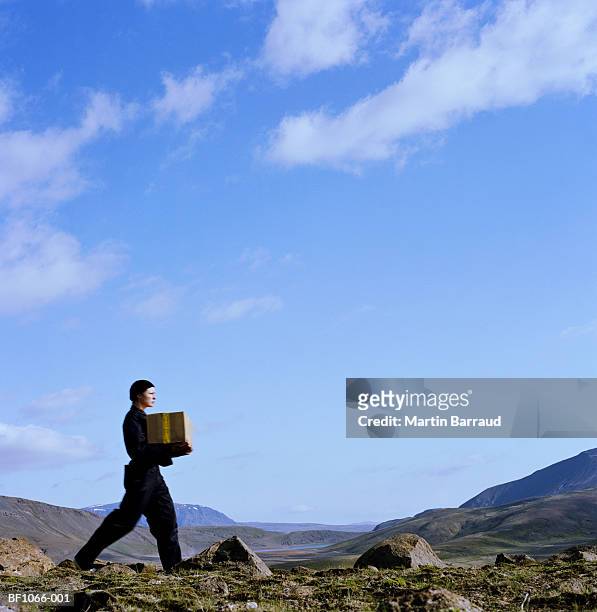 young woman carrying parcel across rocky terrain, profile - kaldidalur stock pictures, royalty-free photos & images
