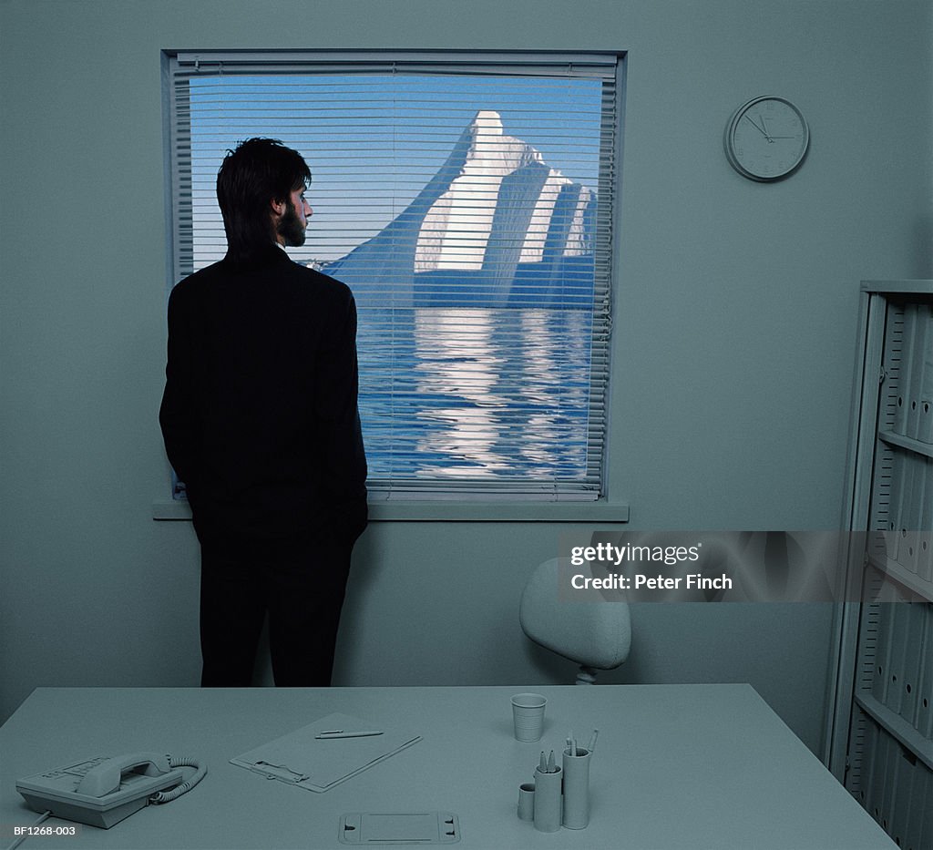 Businessman looking at iceberg through blinds