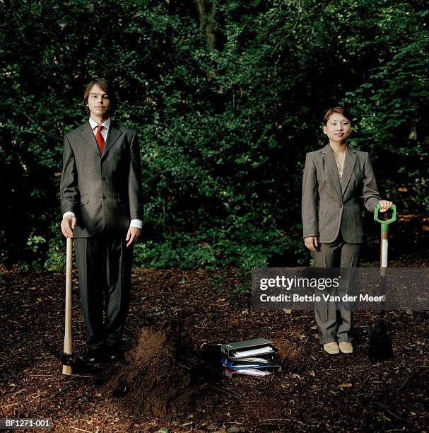 businessman and woman in woods with spades burying files, portrait - bury fotografías e imágenes de stock