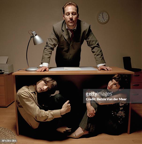 young colleagues hiding under desk from businessman - exploitation foto e immagini stock