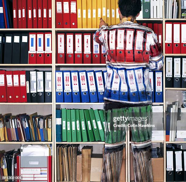 man wearing camouflage suit matching shelves of folders - onzichtbaar stockfoto's en -beelden