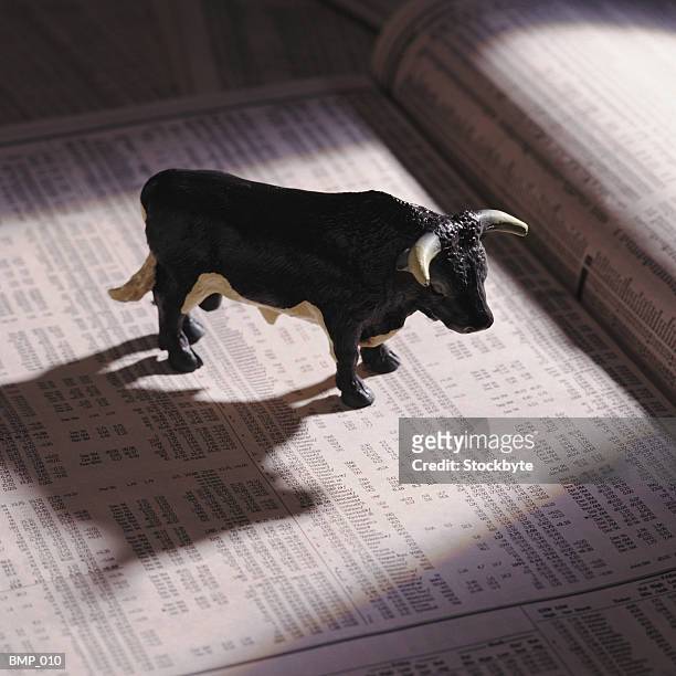 toy bull on newspaper turned to stock listings - paperweight stock pictures, royalty-free photos & images