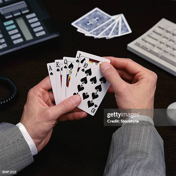 man holding playing cards sitting at desk - zahlenkarte stock-fotos und bilder