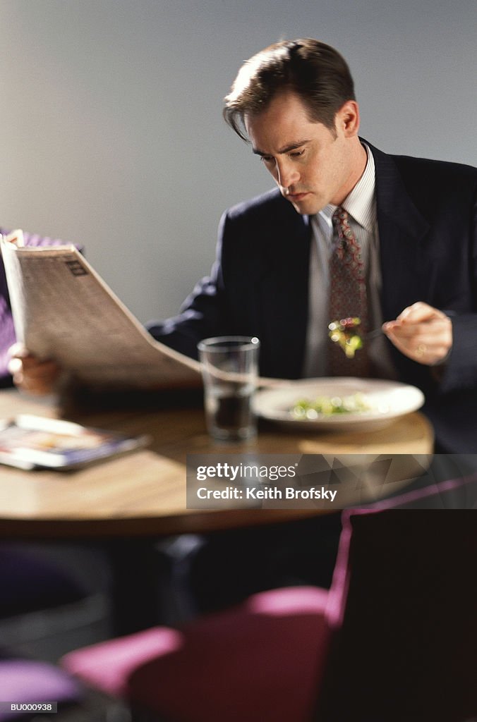 Businessman Reading a Newspaper and Eating