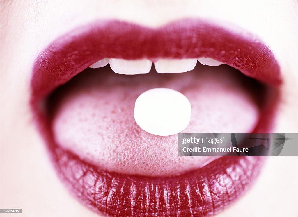 Woman holding pill on tongue, close-up