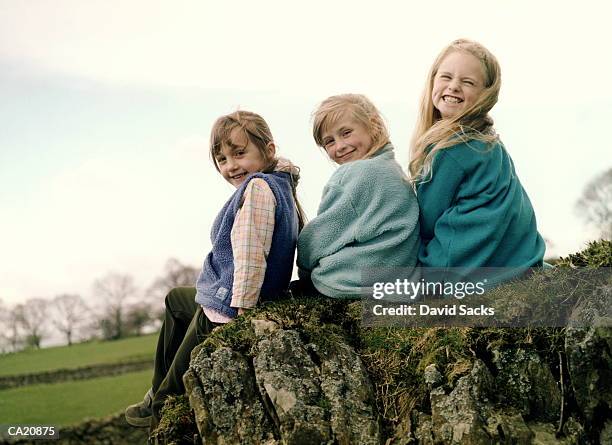 three girls (6-8) sitting on rock looking over shoulder, portrait - endast flickor bildbanksfoton och bilder