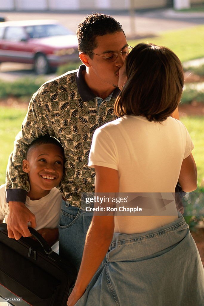 Man greeting woman in front garden watched by son (6-8)