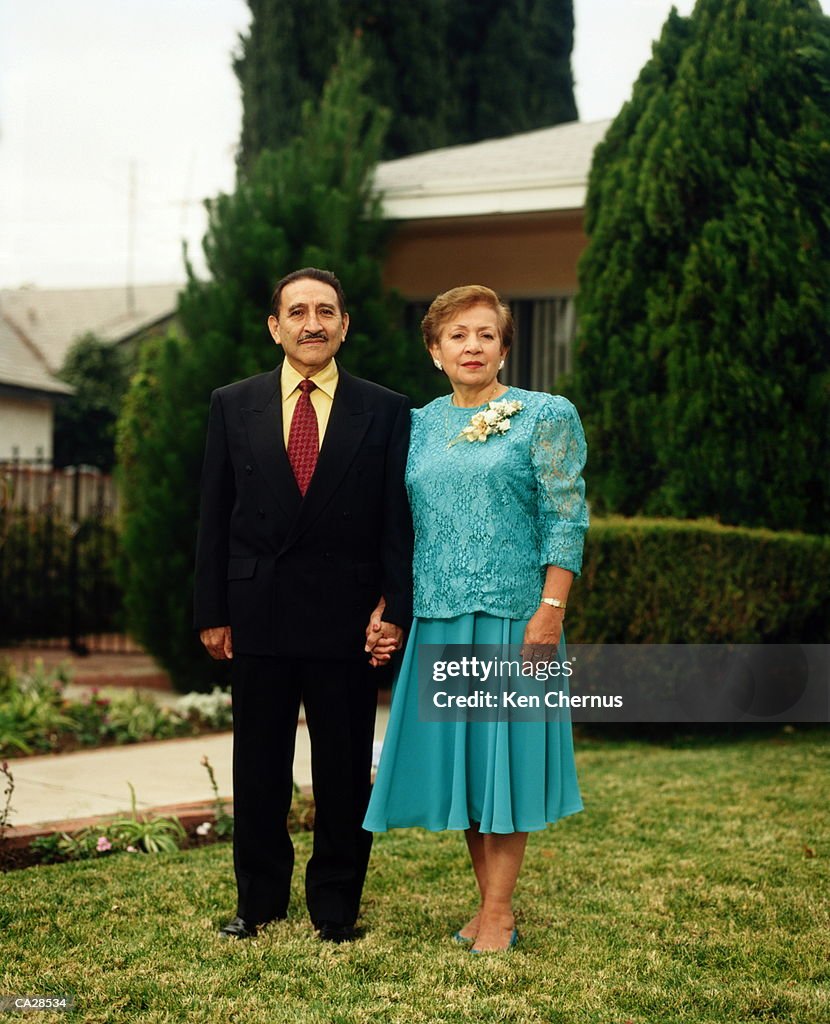 Mature couple standing on grass, holding hands, portrait