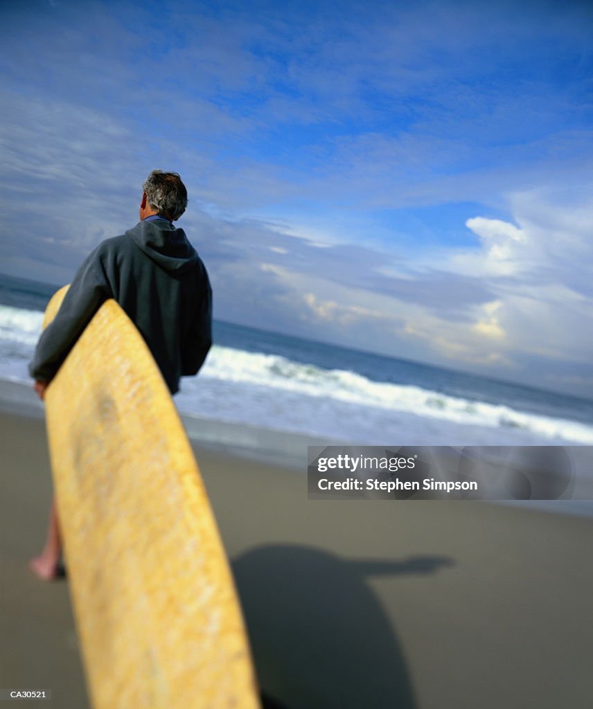 MATURE MAN CARRYING BAMBOO LAMINATE LONGBOARD AT BEACH