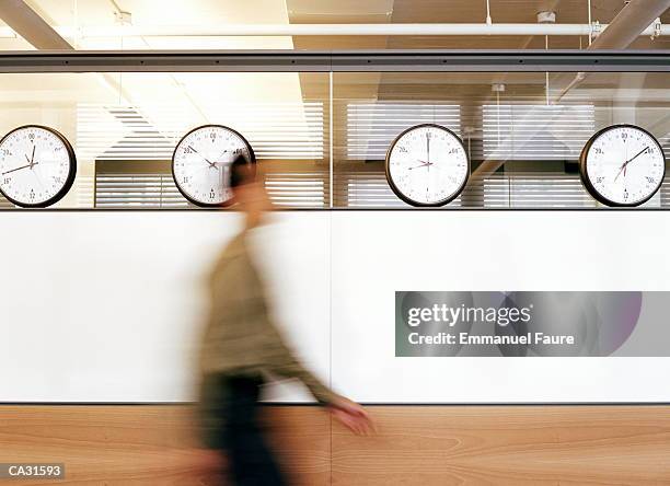 businessman walking by wall clocks showing different time zones - one person time stock-fotos und bilder