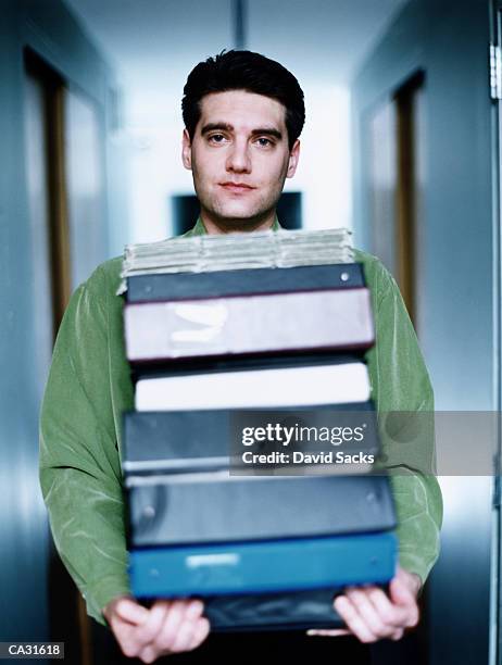 businessman carrying stack of binders in corridor, portrait - binders stockfoto's en -beelden