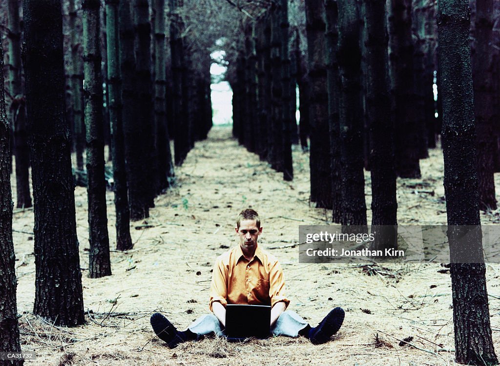 Man sitting on forest floor using laptop computer