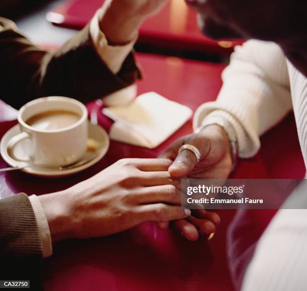 young couple holding hands in restaurant (focus on hands) - emmanuel stock pictures, royalty-free photos & images