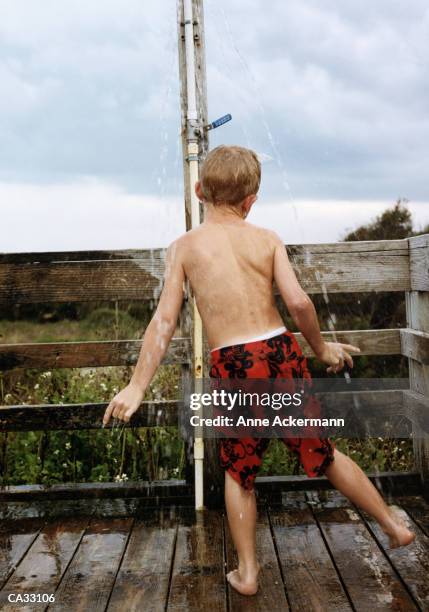 boy (10-12) showering under faucet on boardwalk - anne gergen stock-fotos und bilder