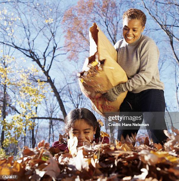 mother pouring bag of autumn leaves over daughter - hans neleman stockfoto's en -beelden