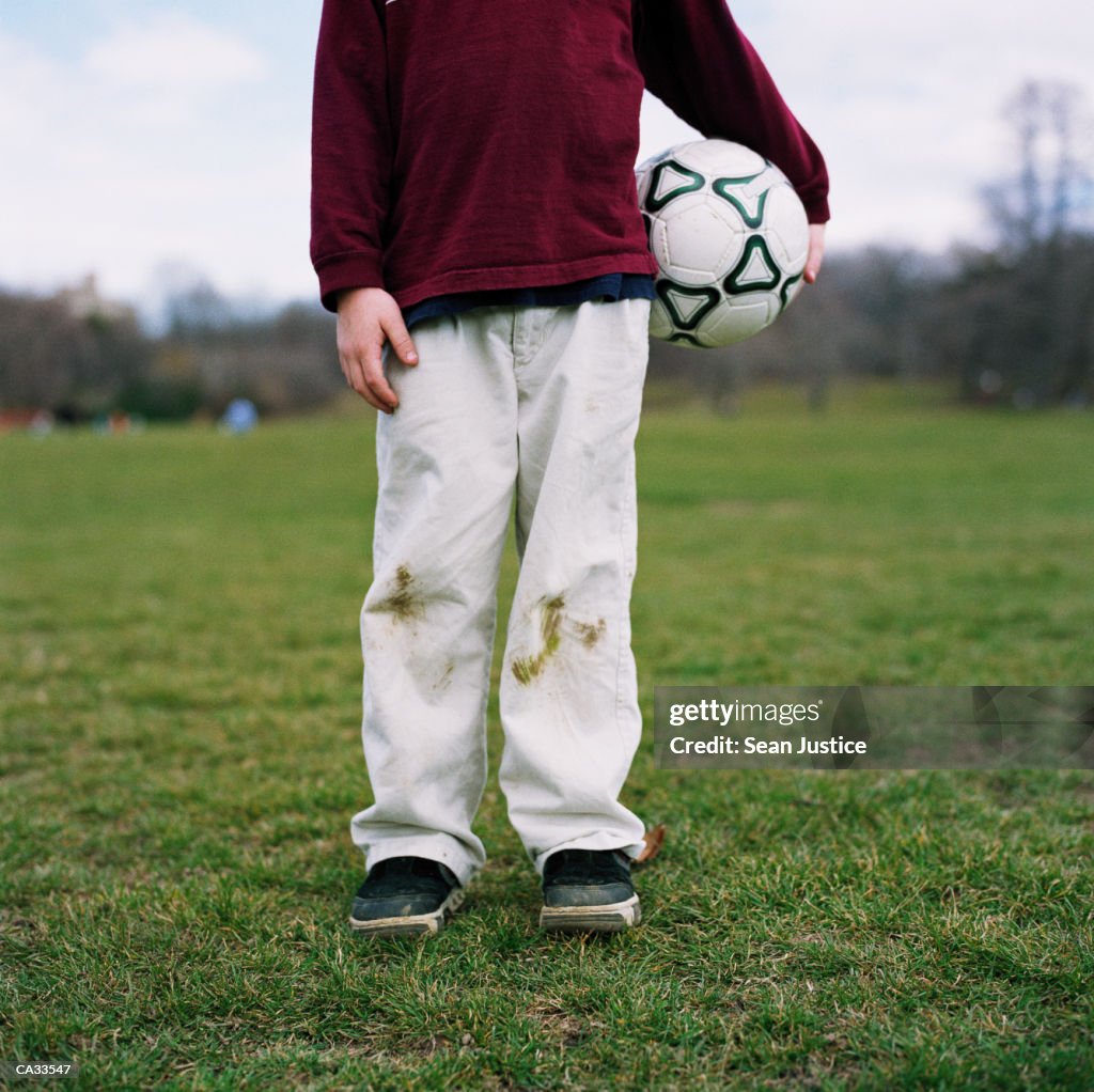 Boy (7-9) holding soccer ball on field, low section