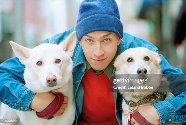 young man hugging two dogs, portrait, close-up - leland bobbe foto e immagini stock