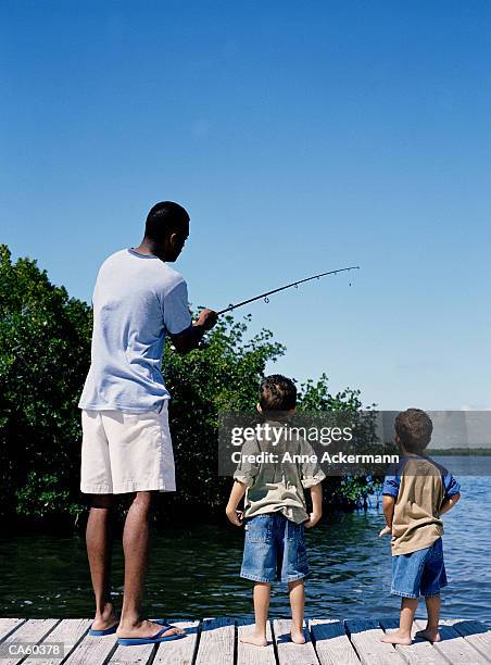 father showing sons (3-5) how to fish, rear view - anne gergen stock-fotos und bilder