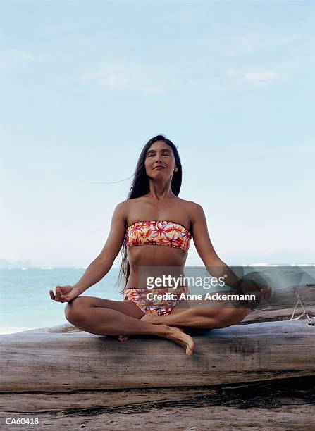 woman sitting with legs crossed on log, meditating - anne gergen stock-fotos und bilder