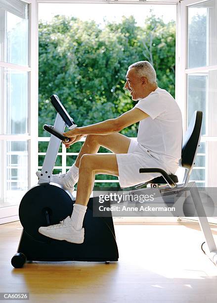 mature man using stationary exercise equipment - anne gergen stock-fotos und bilder