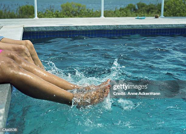 couple sitting at poolside splashing in water, low section - anne gergen stock-fotos und bilder