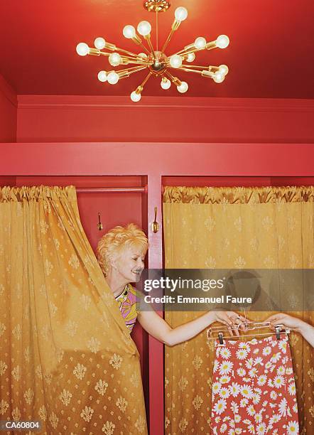 mature woman in dressing room being handed a skirt - camerino di prova foto e immagini stock