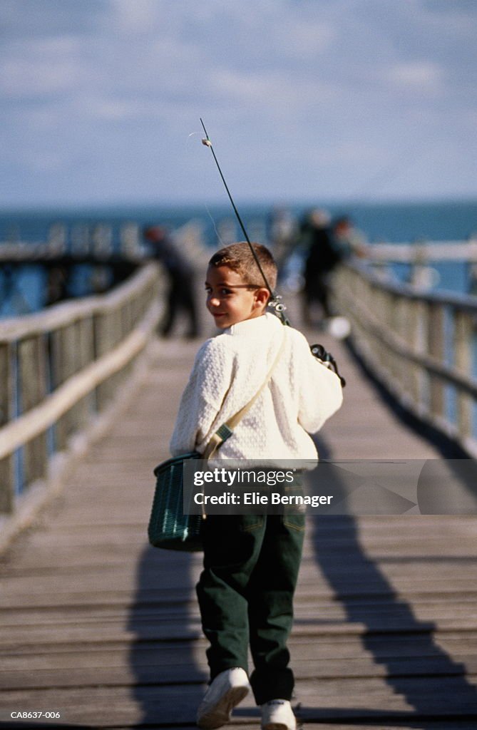 Boy (6-8) walking on jetty, carrying fishing rod