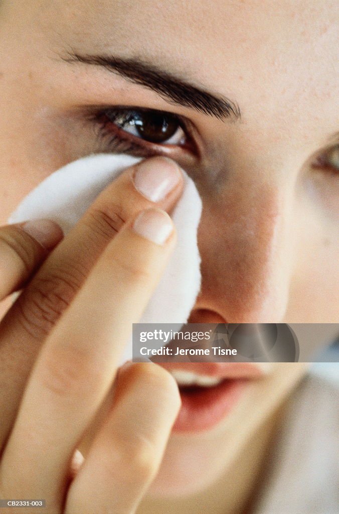 Young woman removing make-up from eye area, close-up