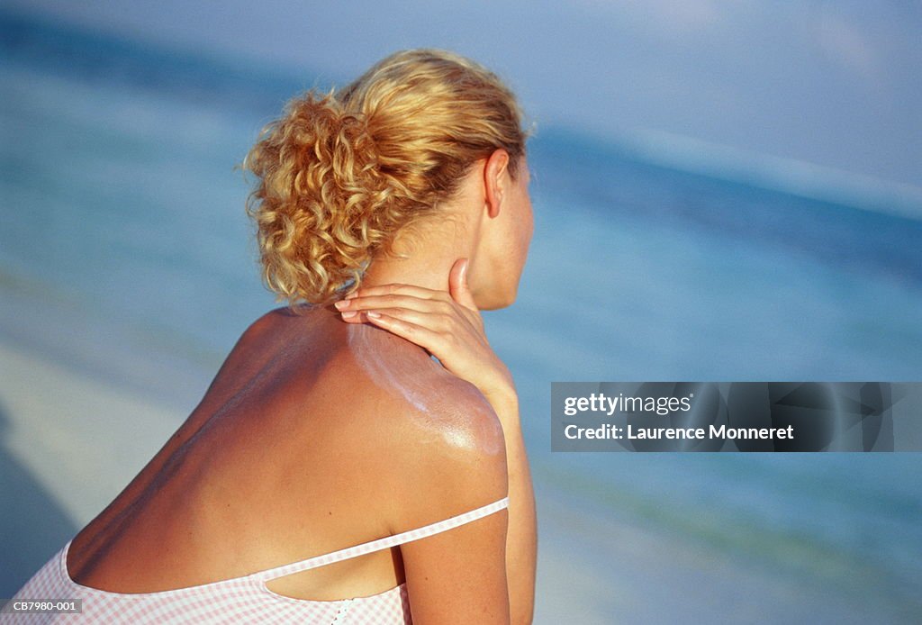 Young woman on beach, applying sun protection to shoulders