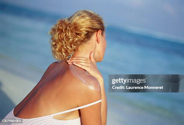 young woman on beach, applying sun protection to shoulders - sunburned 個照片及圖片檔