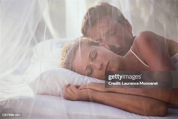 young couple sleeping in bed, view through mosquito net - mosquito netting stock pictures, royalty-free photos & images