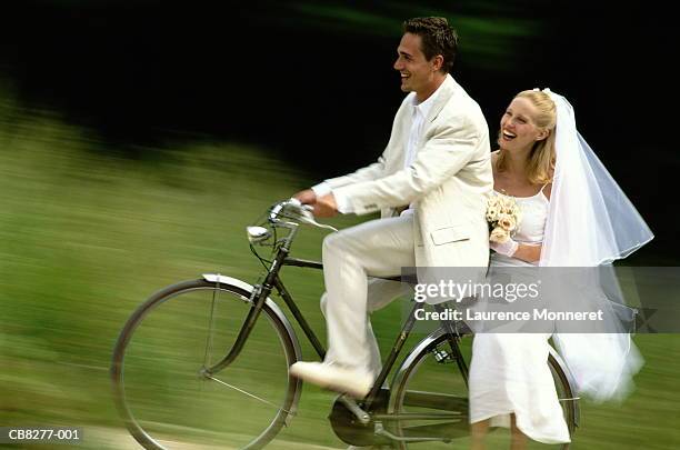 young bride and groom riding bicycle, smiling (blurred motion) - hochzeitspärchen fahrrad stock-fotos und bilder