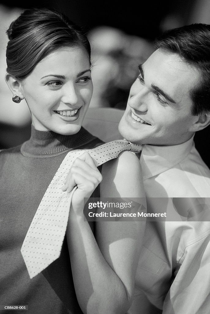 Young couple, woman pulling man's tie, close-up (B&W)