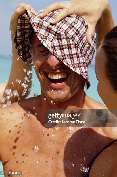 woman putting hat full of water on man's head, on beach, close-up - bucket hat stock pictures, royalty-free photos & images