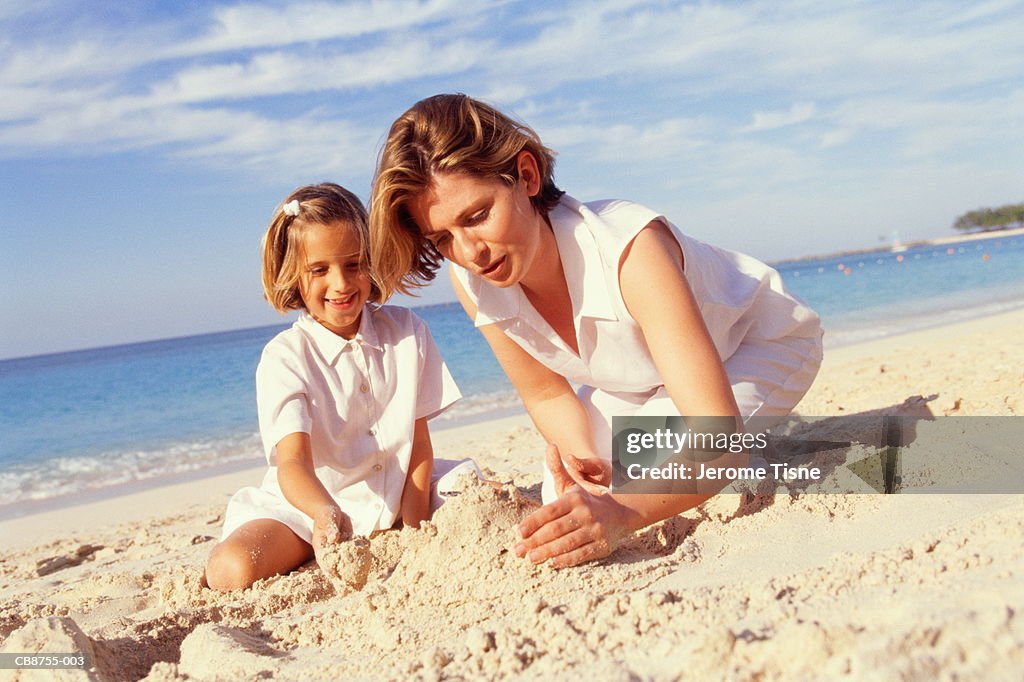 Mother and daughter (6-8) building sandcastle on beach