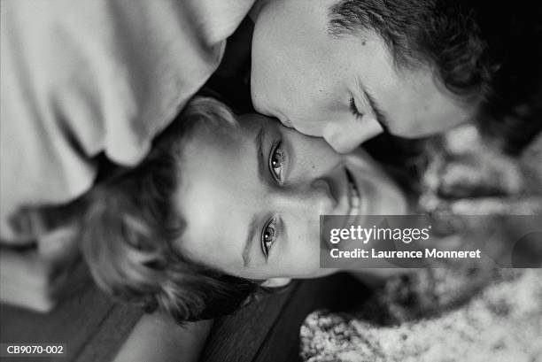 teenagers (15-17) lying on floor, boy kissing girl's cheek (b&w) - tcs stock pictures, royalty-free photos & images